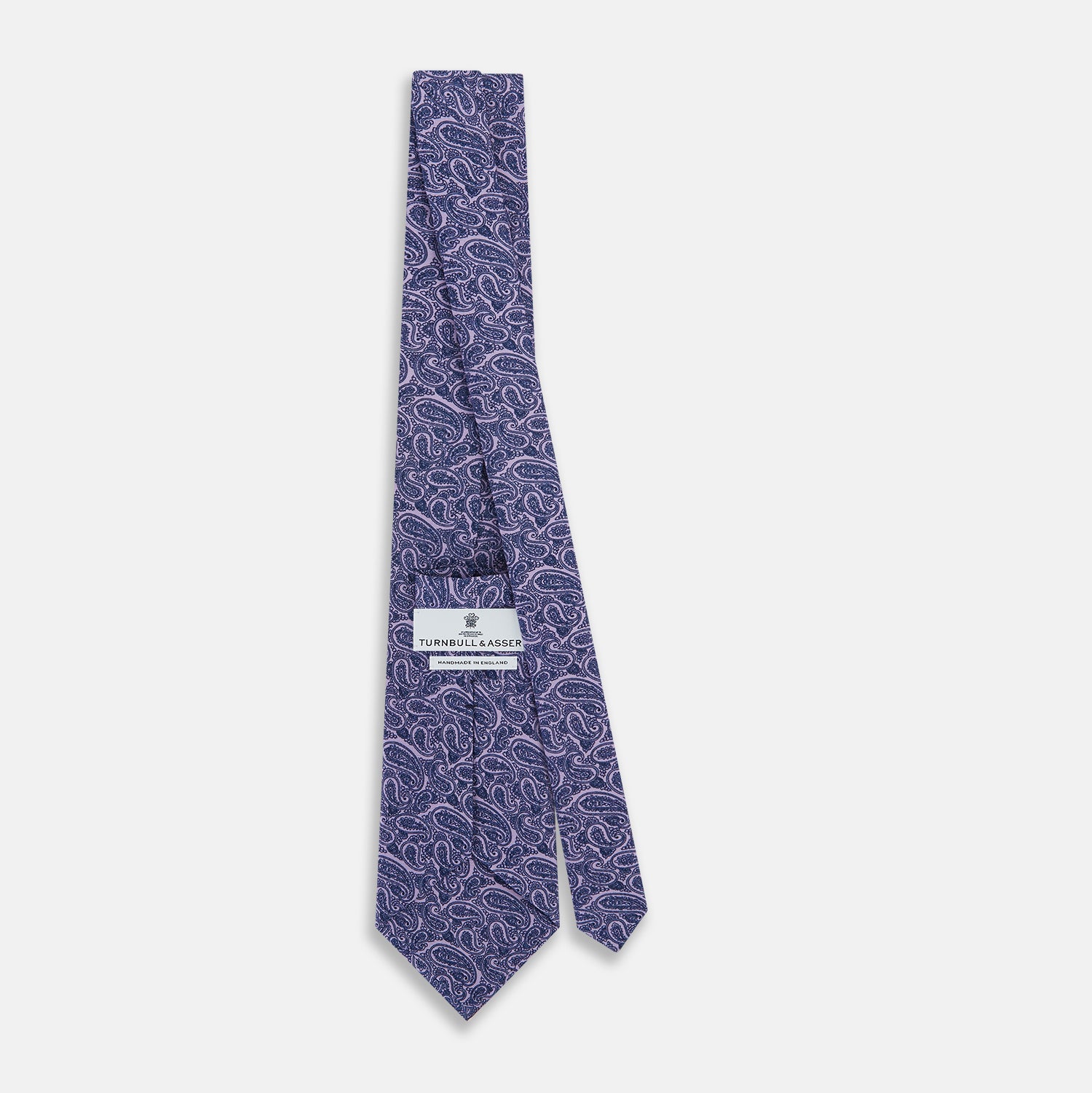 View 4 of product The Turnbull & Asser Lilac Paisley Silk Tie, crafted in England, features a blue paisley pattern on a lilac background and is shown rolled up against a white surface.