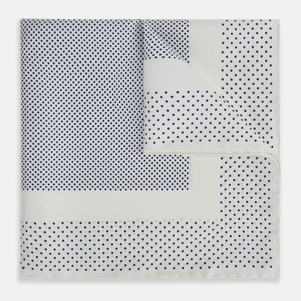 The Turnbull & Asser Cream Dot Silk Pocket Square features a neatly folded pure silk design with a border and center pattern of small navy blue polka dots, displayed on a plain white background.