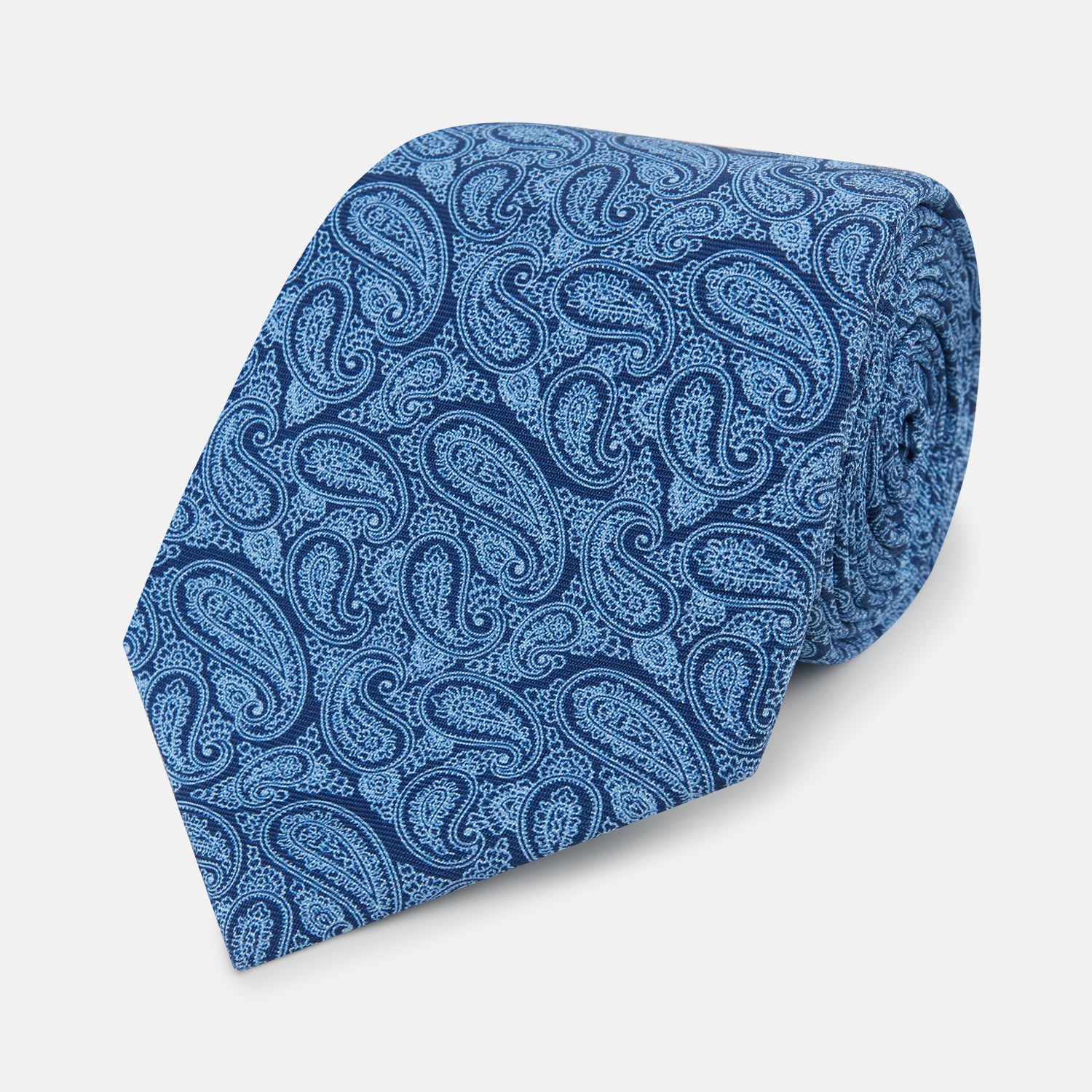 View 1 of product The Turnbull & Asser Azzurro Paisley Silk Tie showcases an intricate light blue paisley pattern on rich blue silk, presented rolled up on a white background.