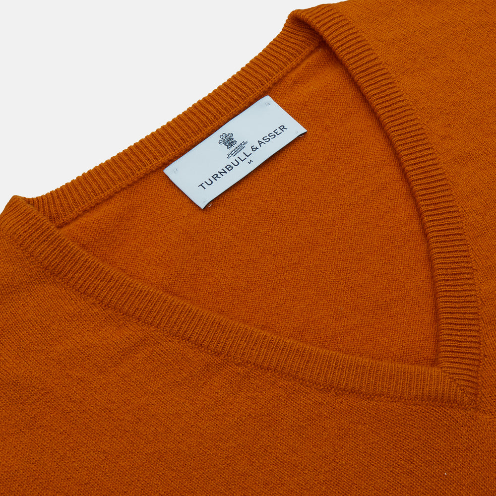 The Turnbull & Asser Rust Paden V-Neck Jumper, a pure cashmere sweater with long sleeves and ribbed cuffs and hem, is laid flat on a white background with the label visible at the neck.