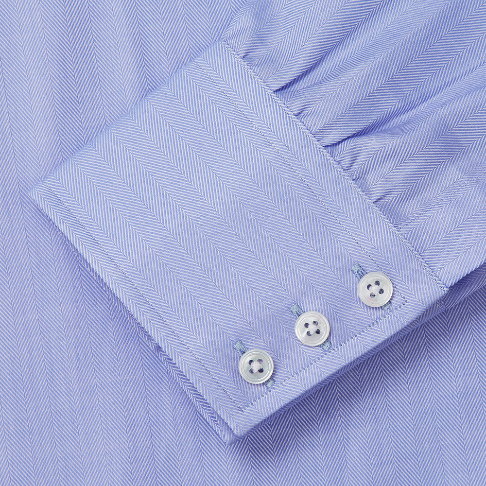 The Turnbull & Asser Blue Herringbone Regular Fit Shirt features a classic Kent collar, long sleeves, white buttons, and buttoned cuffs. Displayed on a white background, it's the perfect formal shirt for any occasion.