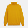 View 2 of product A man with short hair and a beard wears the Gold Aubrey Cashmere Roll Neck Jumper by Turnbull & Asser with dark pants, standing against a plain beige background and calmly looking at the camera, highlighting this stylish autumn sweater look.