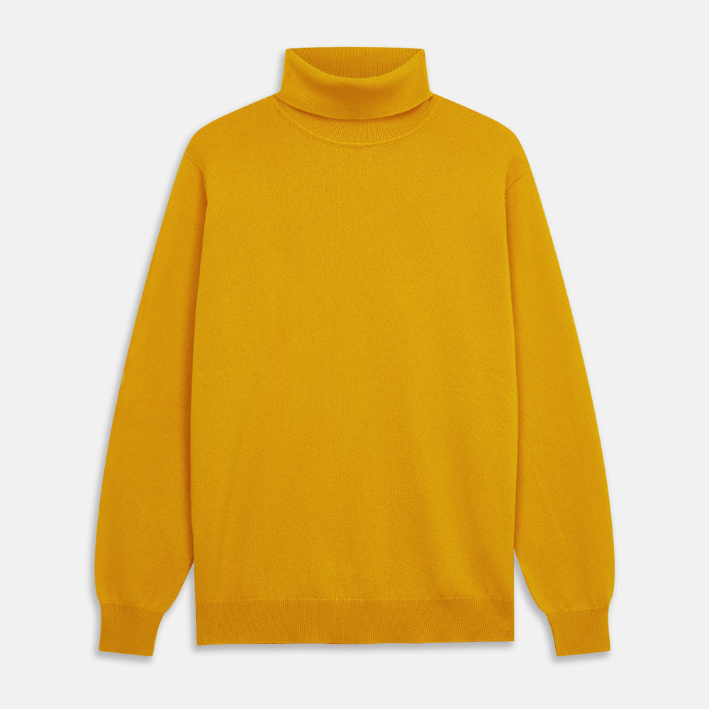 A man with short hair and a beard wears the Gold Aubrey Cashmere Roll Neck Jumper by Turnbull & Asser with dark pants, standing against a plain beige background and calmly looking at the camera, highlighting this stylish autumn sweater look.