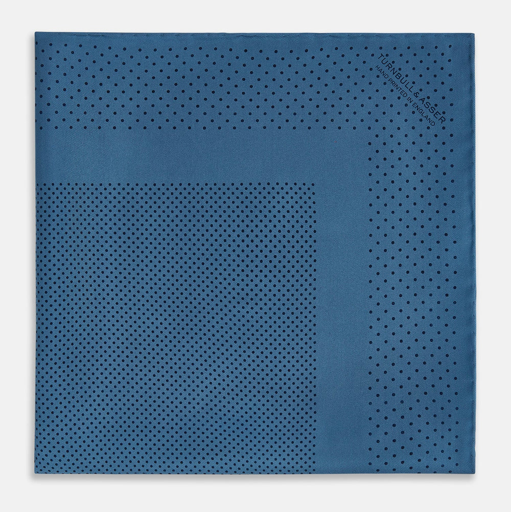 The Blue Dot Silk Pocket Square by Turnbull & Asser features small black polka dots on blue silk and is made in England. The image shows it neatly folded, with a corner turned down to display both sides.