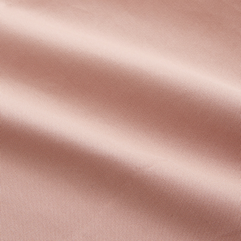 A man faces forward in a relaxed pose against a beige background, wearing the Turnbull & Asser Pink Piece Dyed Weekend Fit Suffolk Shirt with a button-down collar, dark cuffed jeans, and black shoes.