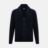 View 1 of product The Turnbull & Asser Midnight Blue Cashmere Shawl Collar Cardigan features ribbed fabric, five black front buttons, a shawl collar, and two front patch pockets, shown against a plain light background.