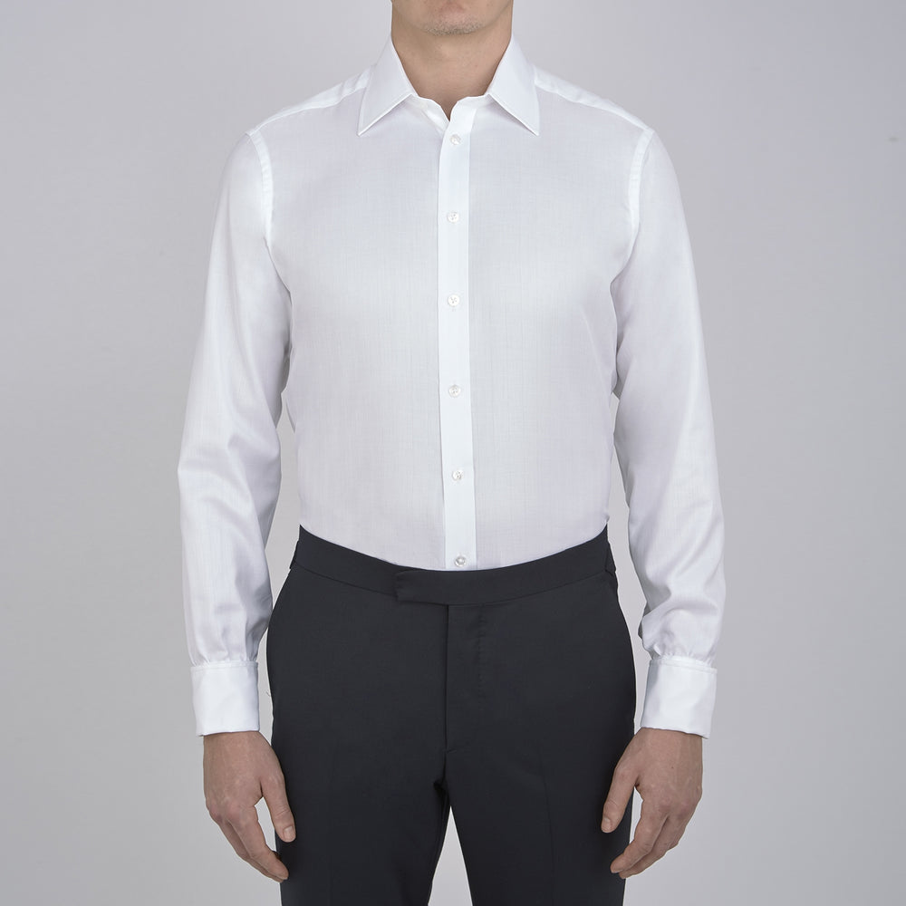 The Turnbull & Asser White Herringbone Superfine Cotton Shirt features a T&A collar, double cuffs, and a visible label inside the collar, shown neatly folded on a light blue background—ideal for minimalist looks or pairing with bold ties.
