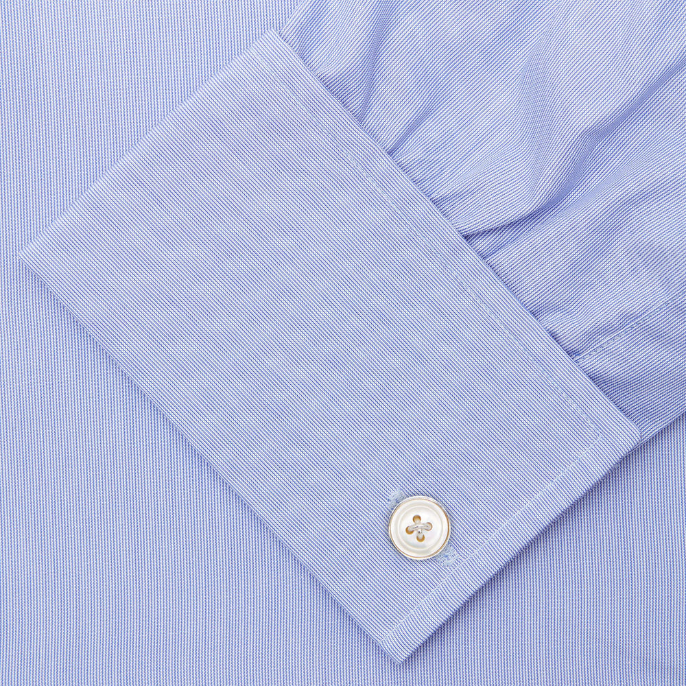 The Turnbull & Asser Blue Hairline Stripe Shirt features a T&A collar, 3-button cuffs, and white buttons. Made from light blue cotton with subtle stripes, it’s neatly folded with the label visible inside the collar on a plain white background.