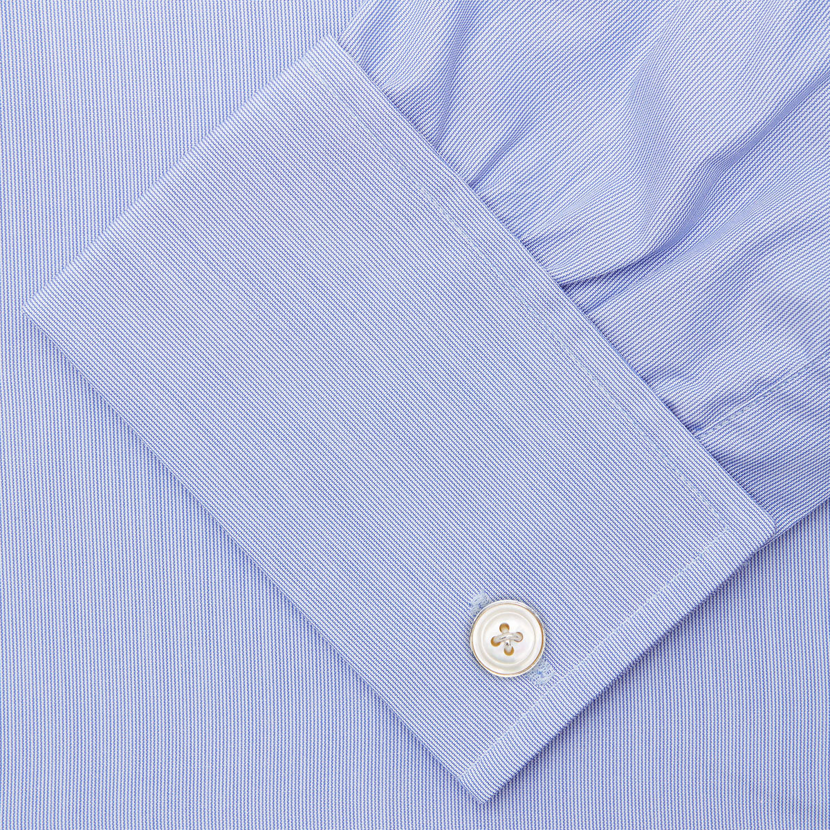 View 6 of product The Turnbull & Asser Blue Hairline Stripe Shirt features a T&A collar, 3-button cuffs, and white buttons. Made from light blue cotton with subtle stripes, it’s neatly folded with the label visible inside the collar on a plain white background.