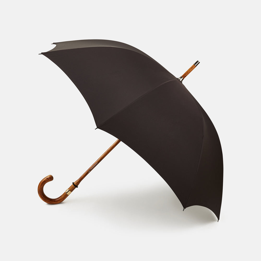 A Black Telescopic Umbrella by Turnbull & Asser with a curved maple handle and shaft, open and angled against a plain white background.