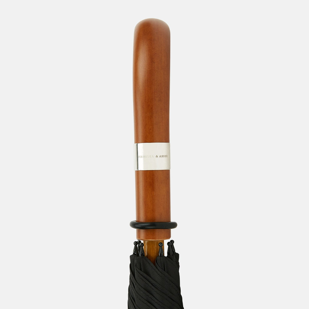 The Turnbull & Asser Black Traveller Umbrella features a Malacca crook handle and straight wooden shaft—a timeless accessory displayed fully opened against a white background.
