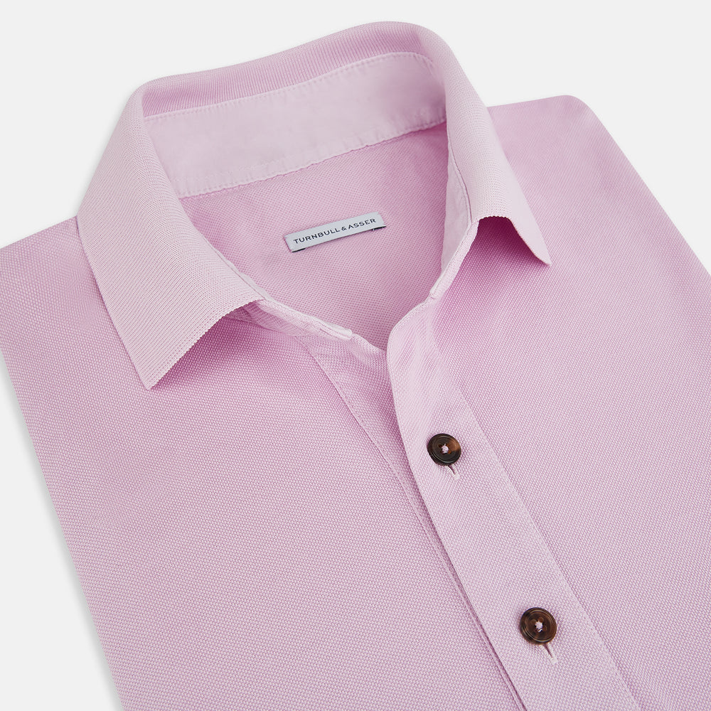 The Turnbull & Asser Pink Polo Shirt is a men's cotton polo with short sleeves, a collar, three dark buttons, and a chest pocket with a button, shown laid flat on a white background.