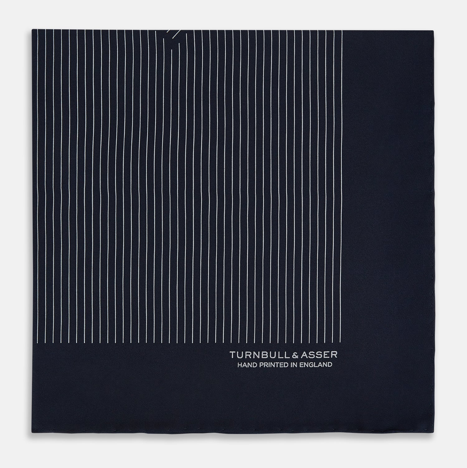 View 3 of product A Navy and Grey Stripe Silk Pocket Square by Turnbull & Asser, featuring hand-rolled edges and brand text in the corner. One corner is folded to show the reverse side.