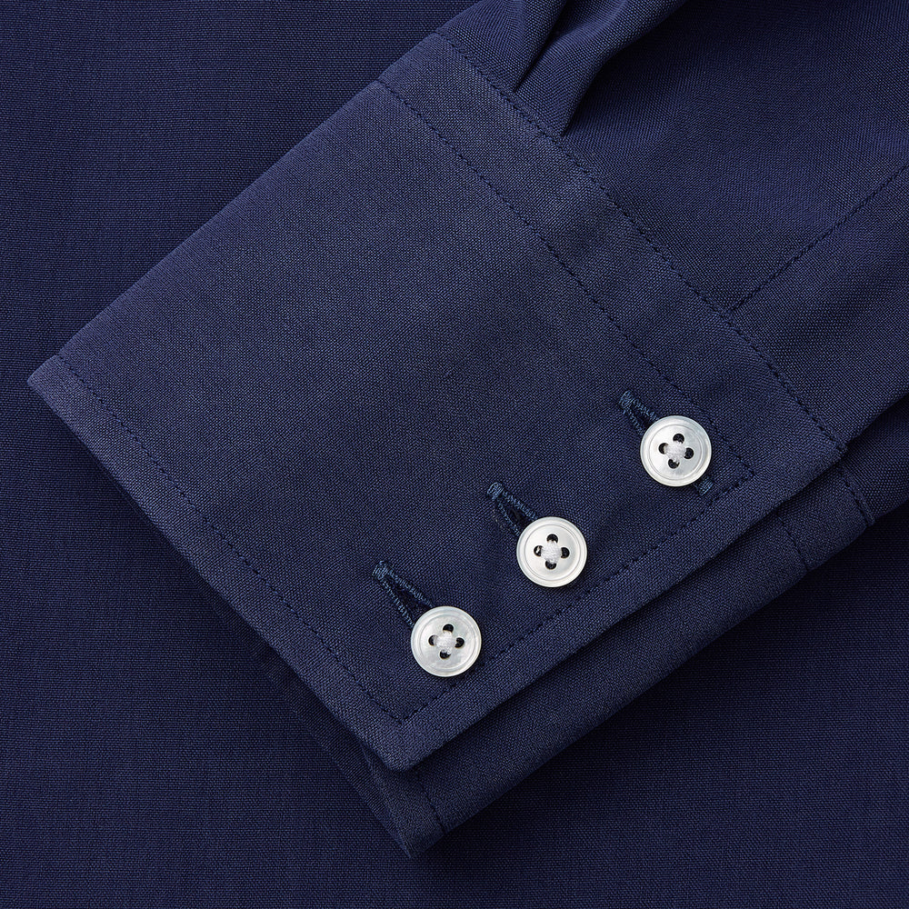 The Turnbull & Asser Blue Soft-touch Silk Lauren Shirt is a navy, long-sleeve button-up with an Igret stand collar, white buttons, curved hem, relaxed fit, and elongated body for a modern look, shown laid flat on a white background.
