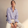 View 5 of product The Turnbull & Asser Pale Blue Candy Stripe Cotton Marlene Shirt is an oversized women's collared shirt with long sleeves, buttoned cuffs, and vertical blue and white stripes, shown laid flat on a white background.