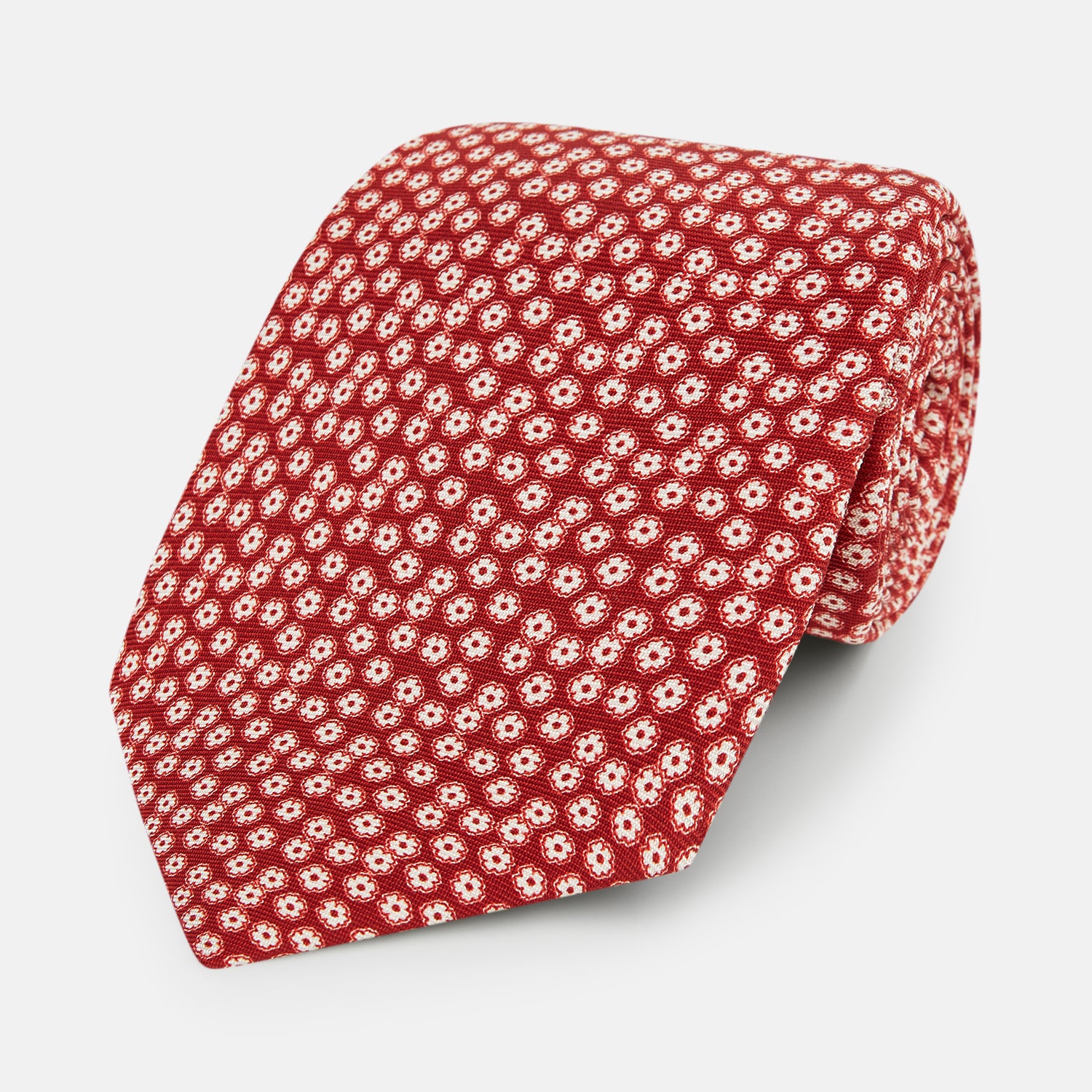 View 1 of product The Red Flower Patterned Silk Tie by Turnbull & Asser, crafted from fine English silk, features a delicate white floral design and is neatly rolled on a white background.