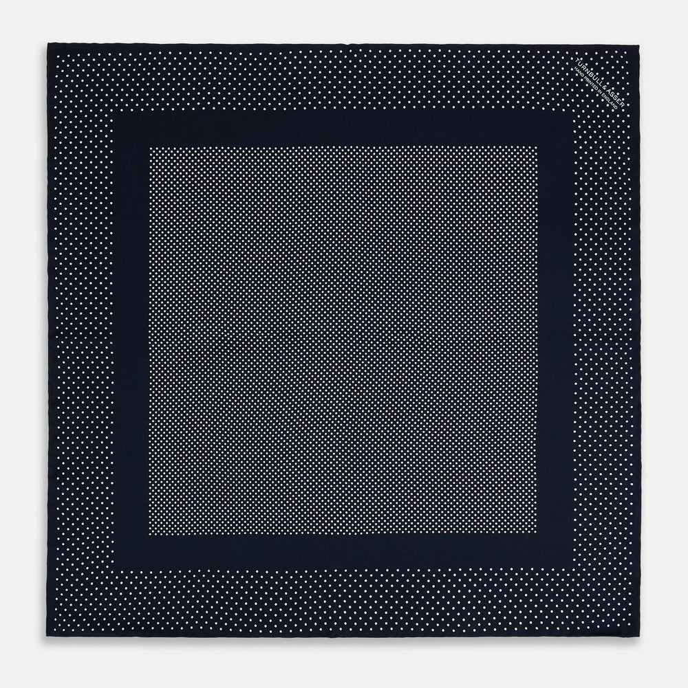The Turnbull & Asser Navy and White Dot Silk Pocket Square features evenly spaced white polka dots on navy, a solid navy border, and one folded corner to reveal the reverse side, highlighting its fine handmade craftsmanship.