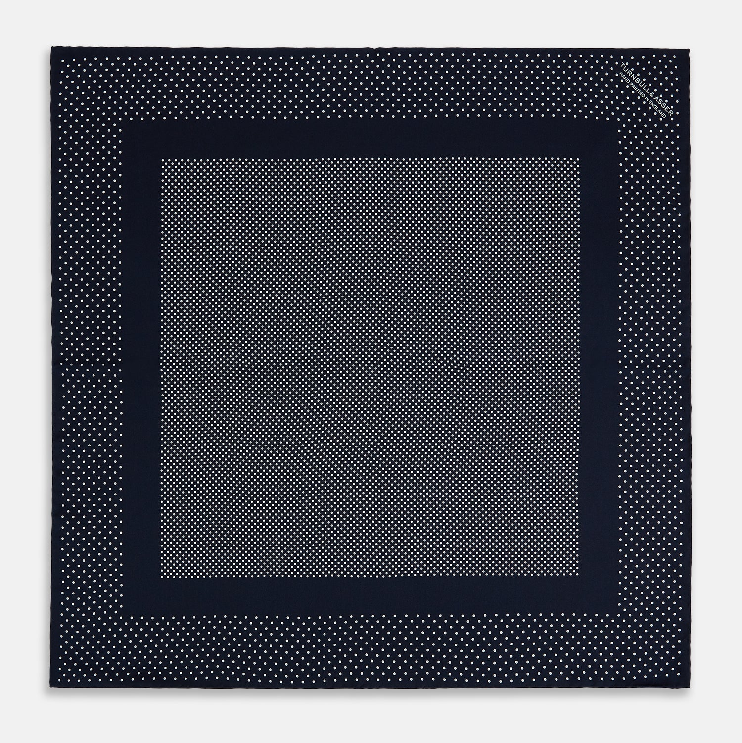 View 4 of product The Turnbull & Asser Navy and White Dot Silk Pocket Square features evenly spaced white polka dots on navy, a solid navy border, and one folded corner to reveal the reverse side, highlighting its fine handmade craftsmanship.