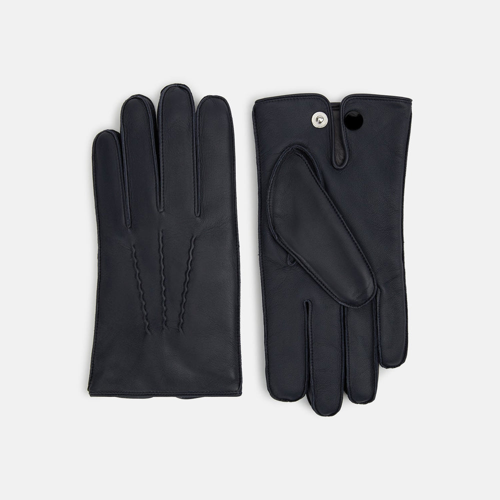 A pair of Turnbull & Asser Navy/Grey Fur-Lined Hairsheep Leather Touchscreen Gloves is displayed on a light background, with one glove showing the palm and the other the back, both featuring simple stitched details and a wrist button closure.