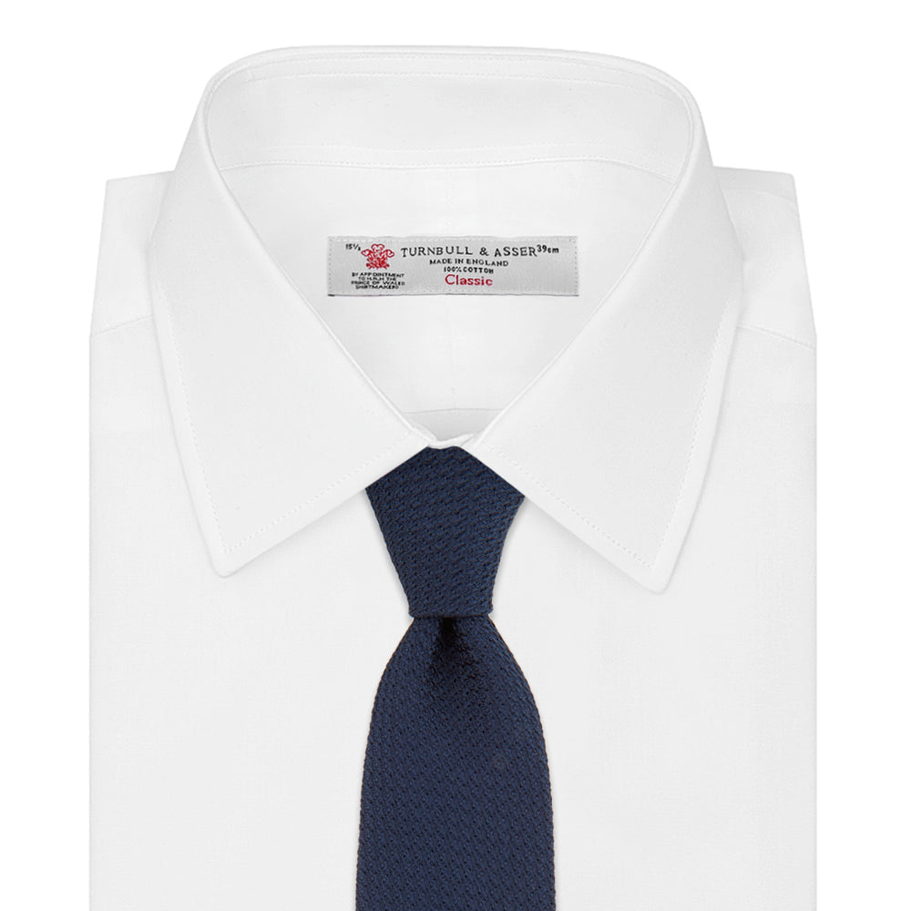 The Turnbull & Asser Navy Plain Woven Grenadine Silk Tie, an essential accessory, is rolled at one end and displayed on a plain white background.