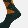 View 4 of product The Forest Green Wool Check Mid-Length Socks by Turnbull & Asser feature a dark green base with orange and brown argyle checks and white dotted lines, shown against a plain white background.