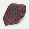 View 1 of product The Turnbull & Asser Burgundy Diamond Silk Tie features a red silk background with a repeating geometric diamond pattern of blue and white squares, exemplifying British craftsmanship.