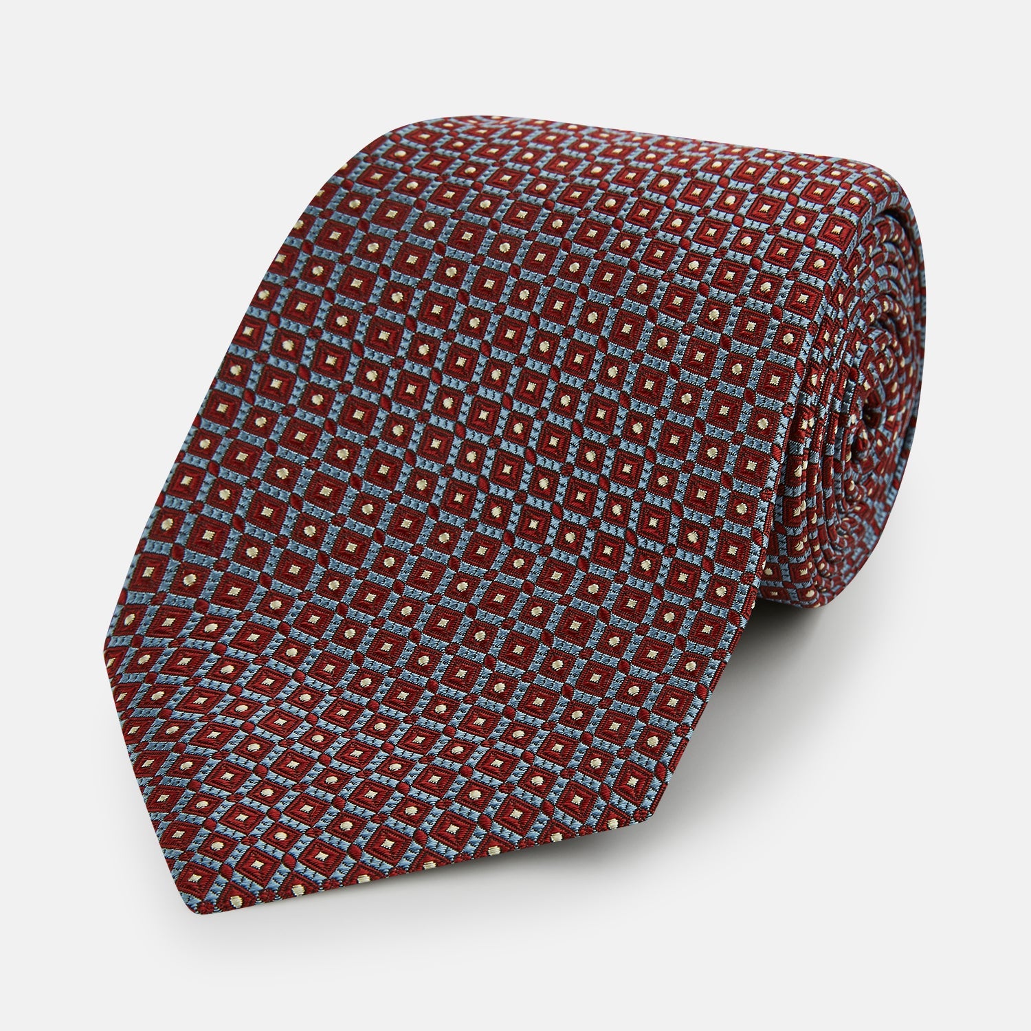 View 1 of product The Turnbull & Asser Burgundy Diamond Silk Tie features a red silk background with a repeating geometric diamond pattern of blue and white squares, exemplifying British craftsmanship.