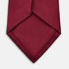 View 4 of product The HORIZONTAL TWILL BURGUNDY TIE by Turnbull & Asser features a subtle textured pattern in solid burgundy, rolled neatly and displayed against a white background—a versatile addition to any gentleman’s wardrobe.