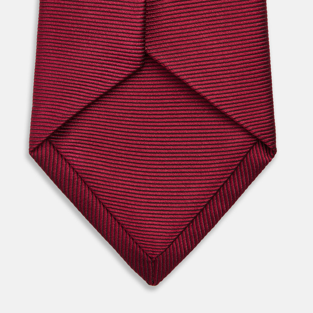 The HORIZONTAL TWILL BURGUNDY TIE by Turnbull & Asser features a subtle textured pattern in solid burgundy, rolled neatly and displayed against a white background—a versatile addition to any gentleman’s wardrobe.