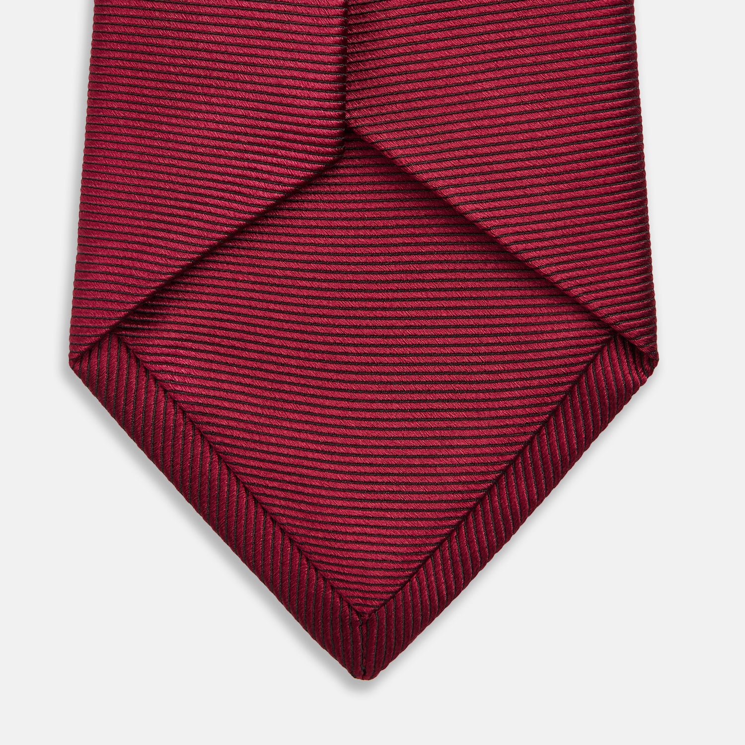View 4 of product The HORIZONTAL TWILL BURGUNDY TIE by Turnbull & Asser features a subtle textured pattern in solid burgundy, rolled neatly and displayed against a white background—a versatile addition to any gentleman’s wardrobe.