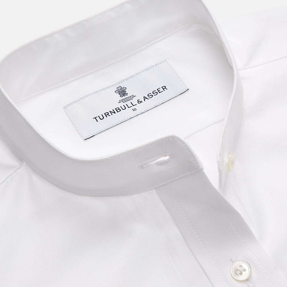 The White Cotton Lauren Shirt by Turnbull & Asser, featuring a stand collar, button-down front, and elongated body, is laid flat on a plain white background.