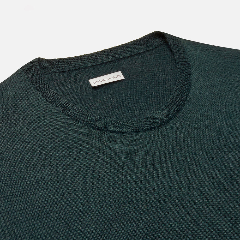 The Turnbull & Asser Forest Green Fine Merino Round Neck Jumper for men is shown on a light gray background. This knitwear features a classic design with ribbed cuffs, hem, and neckline.