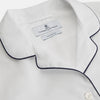 View 2 of product The Turnbull & Asser Women's Harriet Plain White Cotton Pyjama Set features long sleeves, black piping, a chest pocket, and matching pants with elastic waistband and ribbon tie, all displayed on a white background.