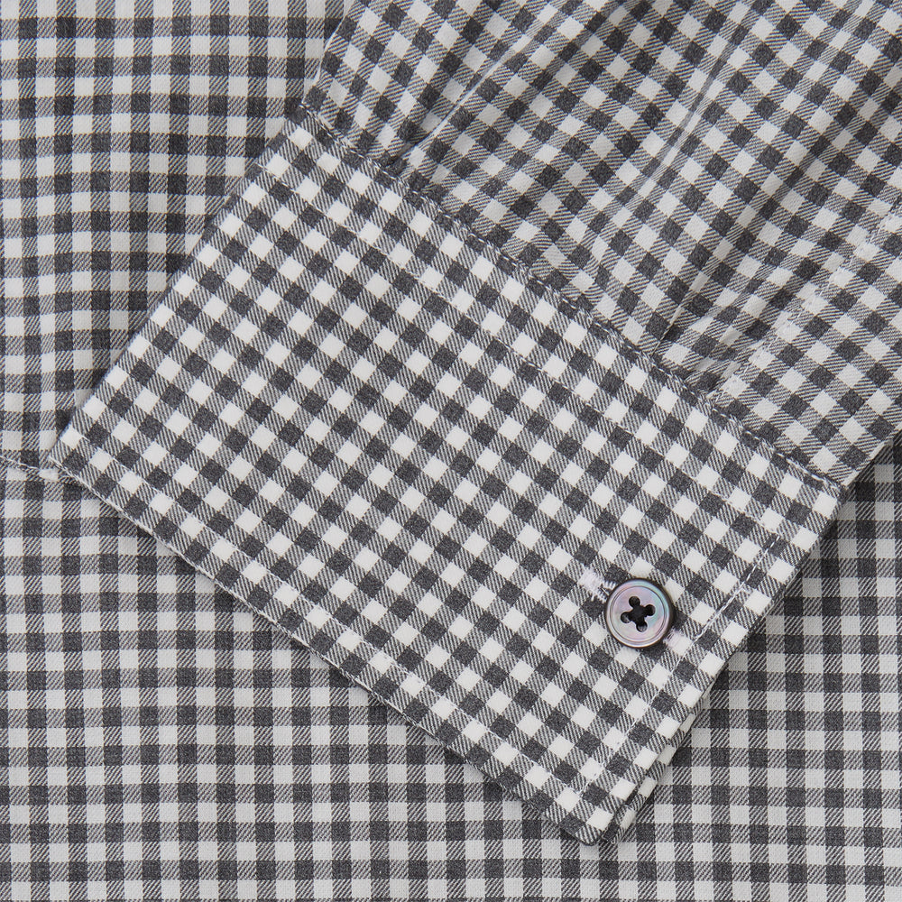 A person with a shaved head models the Turnbull & Asser Grey Check Weekend Fit Flannel Shirt with a Derby collar and 1-button cuffs, sleeves rolled up, paired with dark trousers against a plain background, gazing directly at the camera.