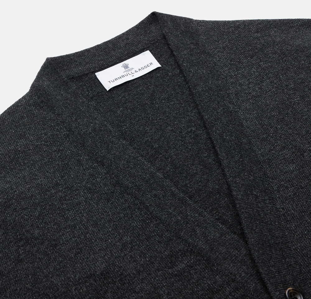 The Turnbull & Asser Charcoal Lachlan Cashmere Cardigan features long sleeves, a V-neck, button-down front, two pockets, and ribbed cuffs—ideal for smart-casual layering—shown laid flat on a white background.