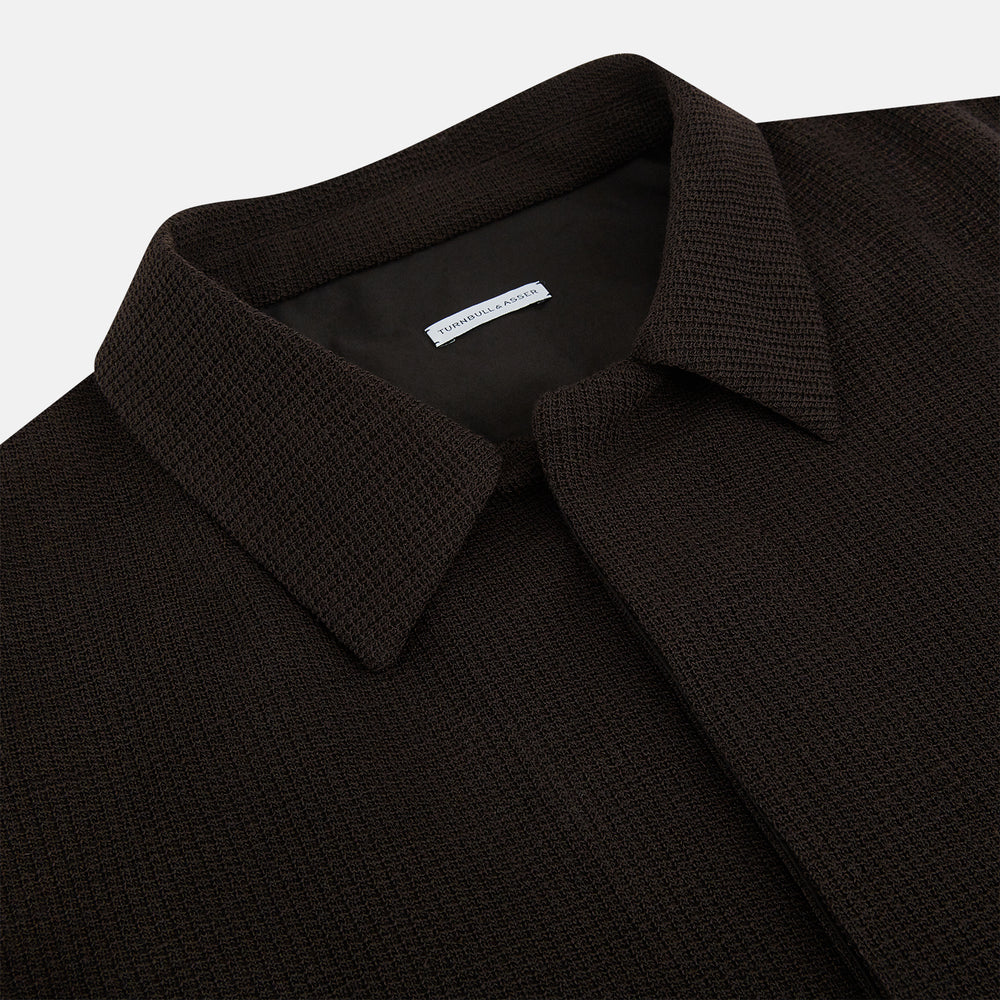 The Turnbull & Asser Dark Chocolate Greenwich Knitted Overshirt is crafted from Italian wool, with a classic collar, two flap chest pockets, and a concealed button front—offering a sleek cardigan alternative. Shown on a white background.