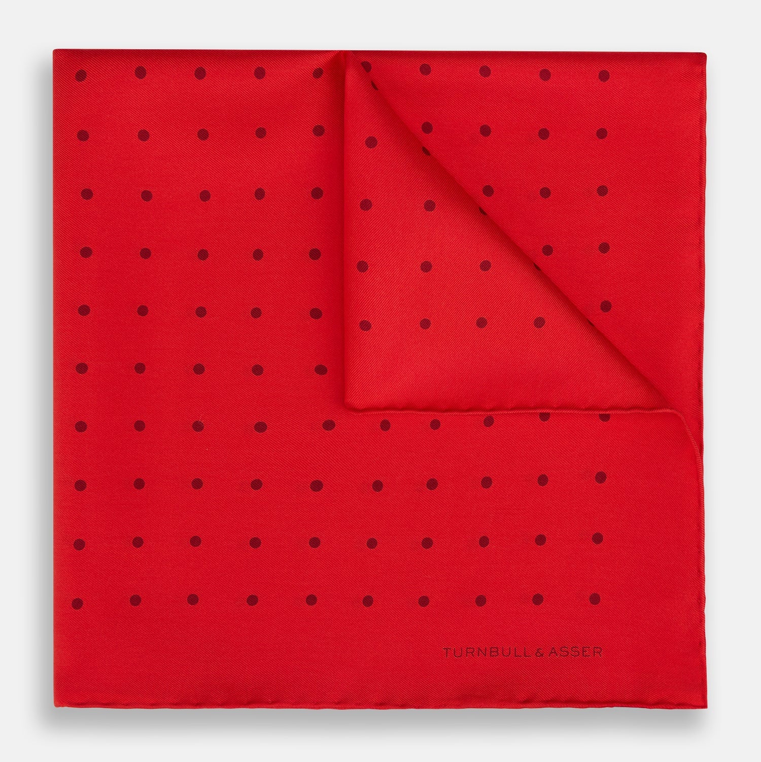 View 1 of product The Turnbull & Asser Red and Burgundy Spot Silk Pocket Square features evenly spaced small spots and the brand logo in the bottom right corner—perfect for formal wear. One corner is folded to show the reverse side.