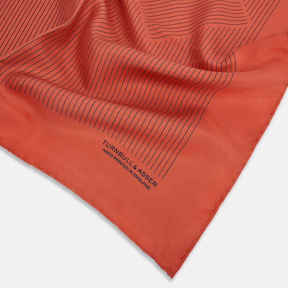 The Orange Stripe Silk Pocket Square by Turnbull & Asser features thin black vertical lines and "TURNBULL & ASSER HAND PRINTED IN ENGLAND" in the corner, neatly folded on a white background.