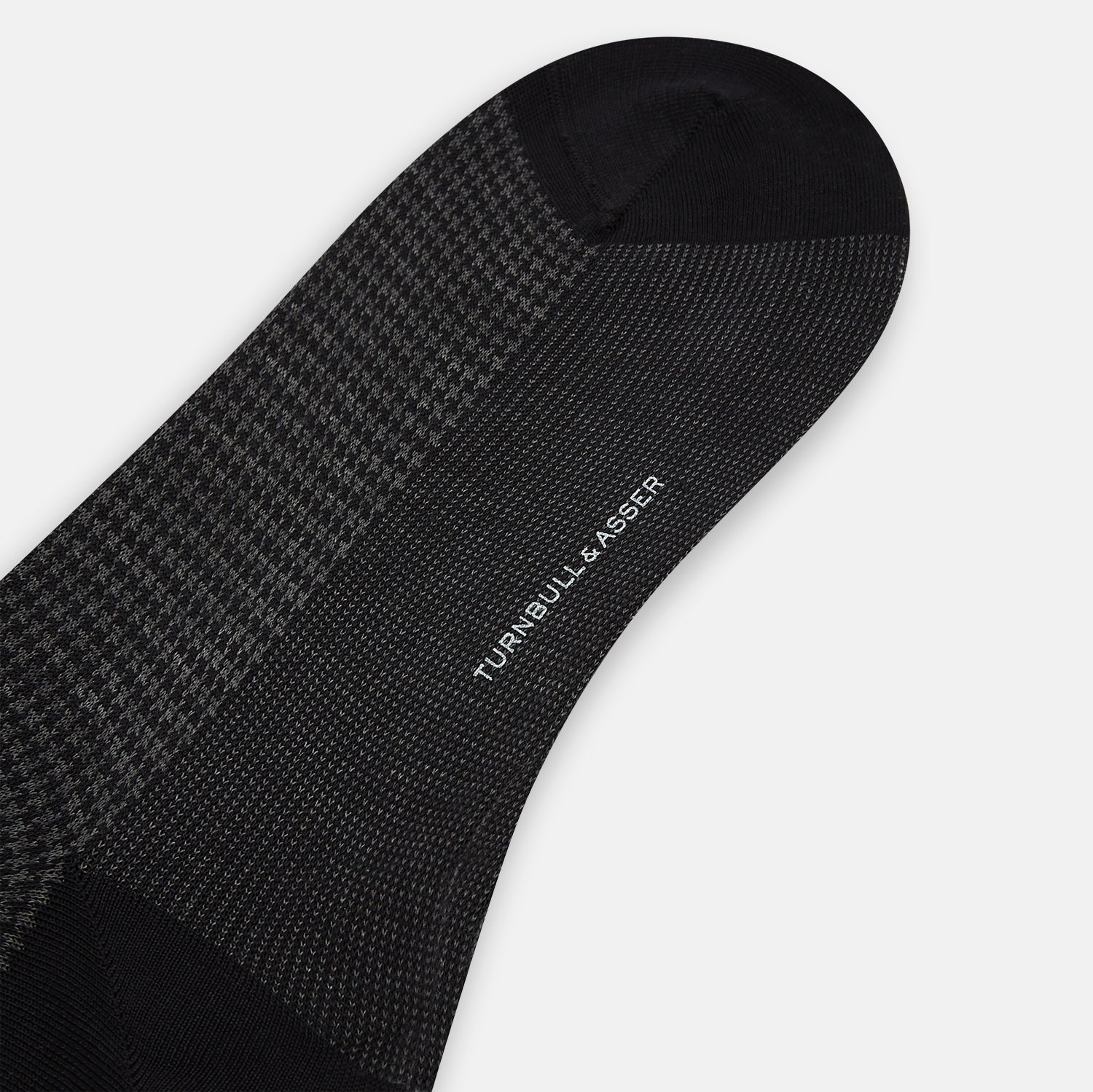 View 3 of product The Turnbull & Asser Charcoal Melange Houndstooth Mid-Length Sock features a black toe, heel, and cuff, and is shown singly against a plain white background.