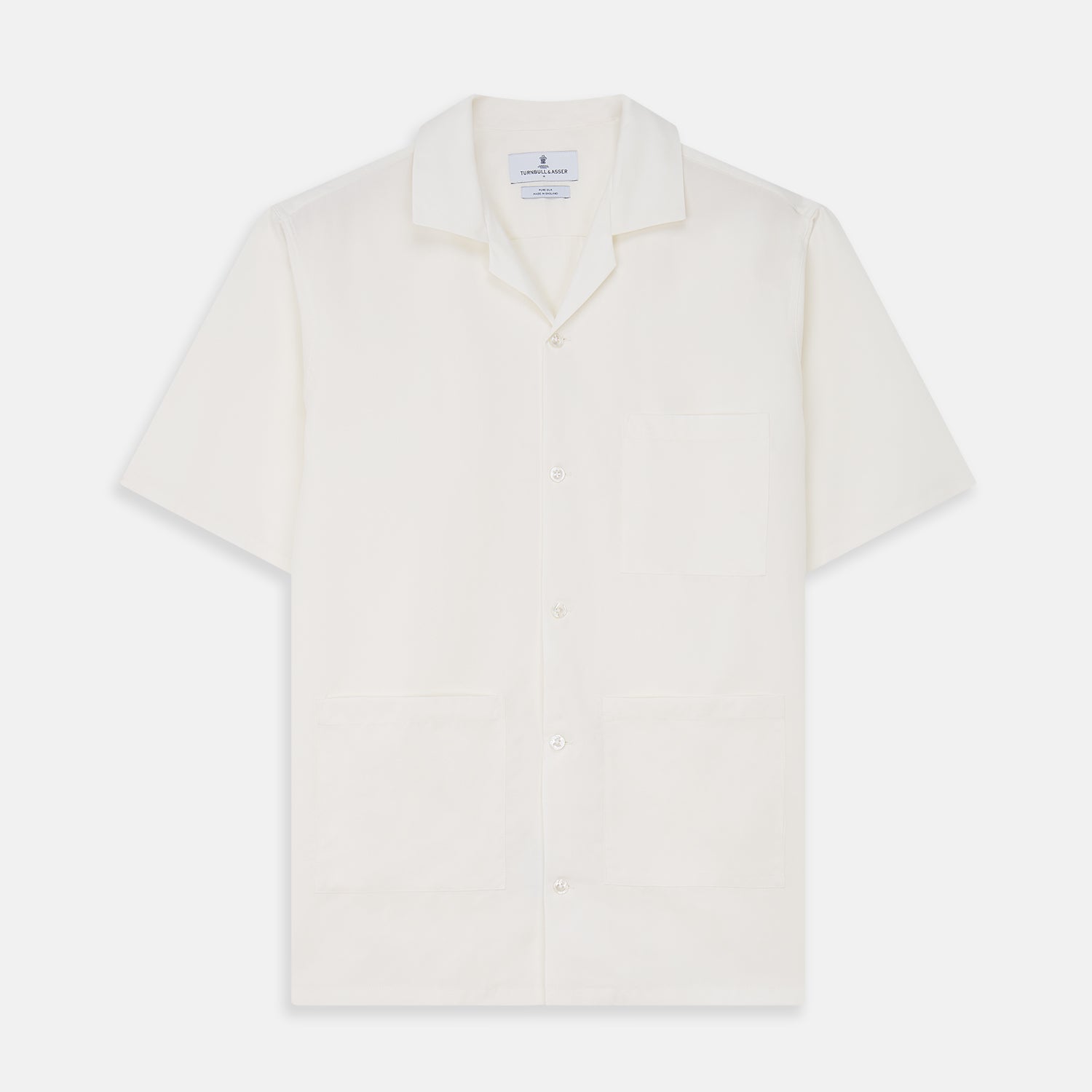 View 1 of product The Cream Silk Holiday Fit Phillips Shirt by Turnbull & Asser is a short-sleeved, collared silk shirt in off-white with three front pockets and a revere collar, displayed flat on a plain white background.