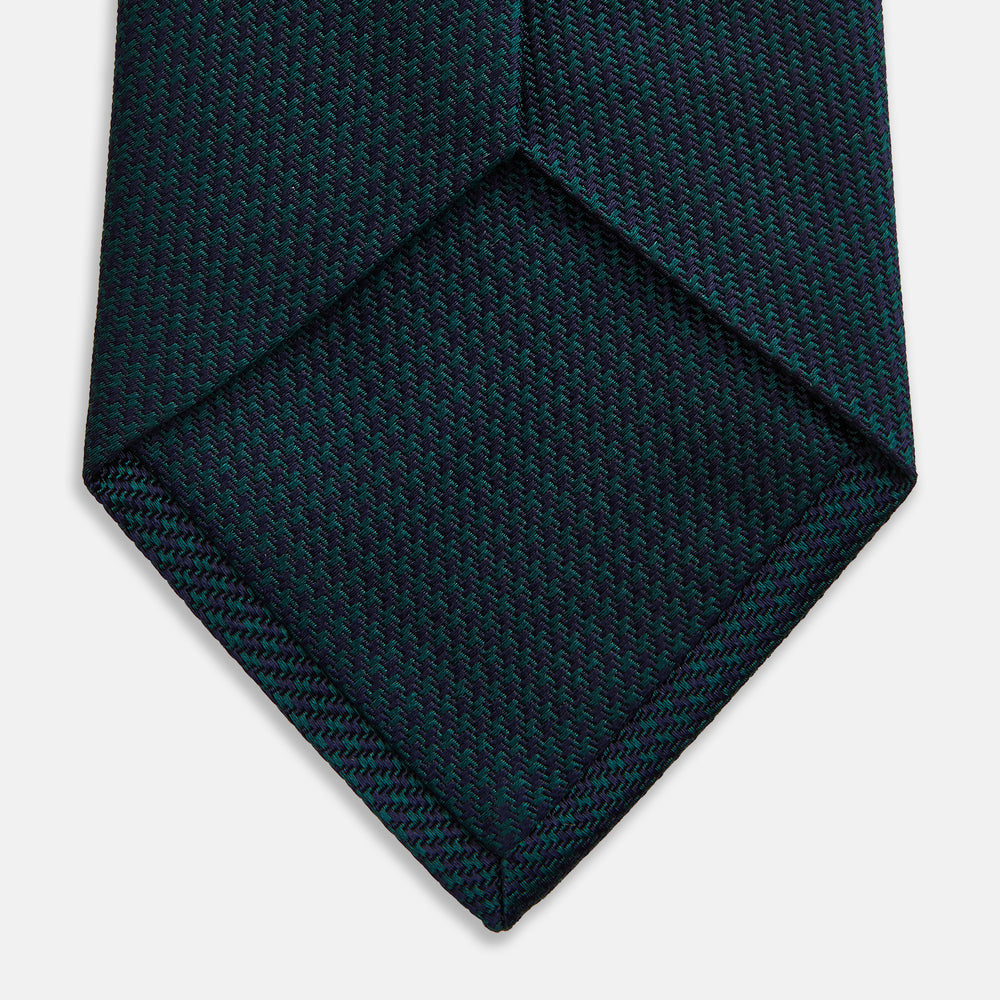The Turnbull & Asser Navy Houndstooth Forest Green Tie is shown rolled up, featuring a subtle houndstooth pattern against a plain white background.