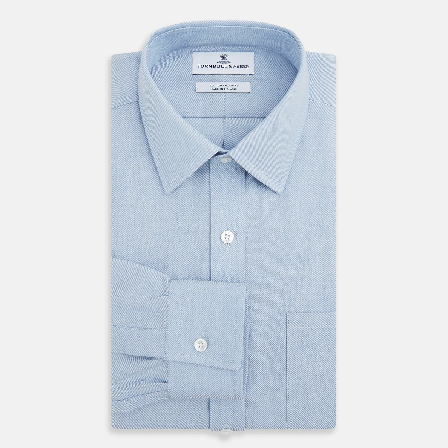 View 4 of product The Turnbull & Asser Pale Blue Cotton Cashmere Derby Collar Richmond Shirt features a soft cotton-cashmere blend, derby collar, white buttons, left chest pocket, and buttoned cuffs, shown laid flat on a white background.