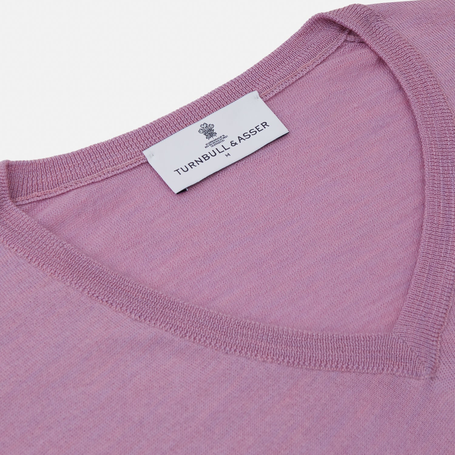 View 2 of product The Pink Merino Kennedy V-Neck Jumper by Turnbull & Asser features long sleeves with ribbed cuffs and waistband, shown on a plain white background—ideal for knitwear lovers.