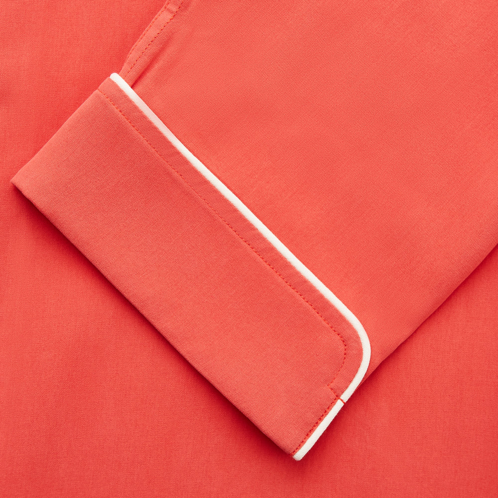 The Turnbull & Asser Women's Coral Pink Silk Thelma Pyjama Set features a long-sleeve button-up top with two front pockets and matching drawstring pants, shown on a white background.