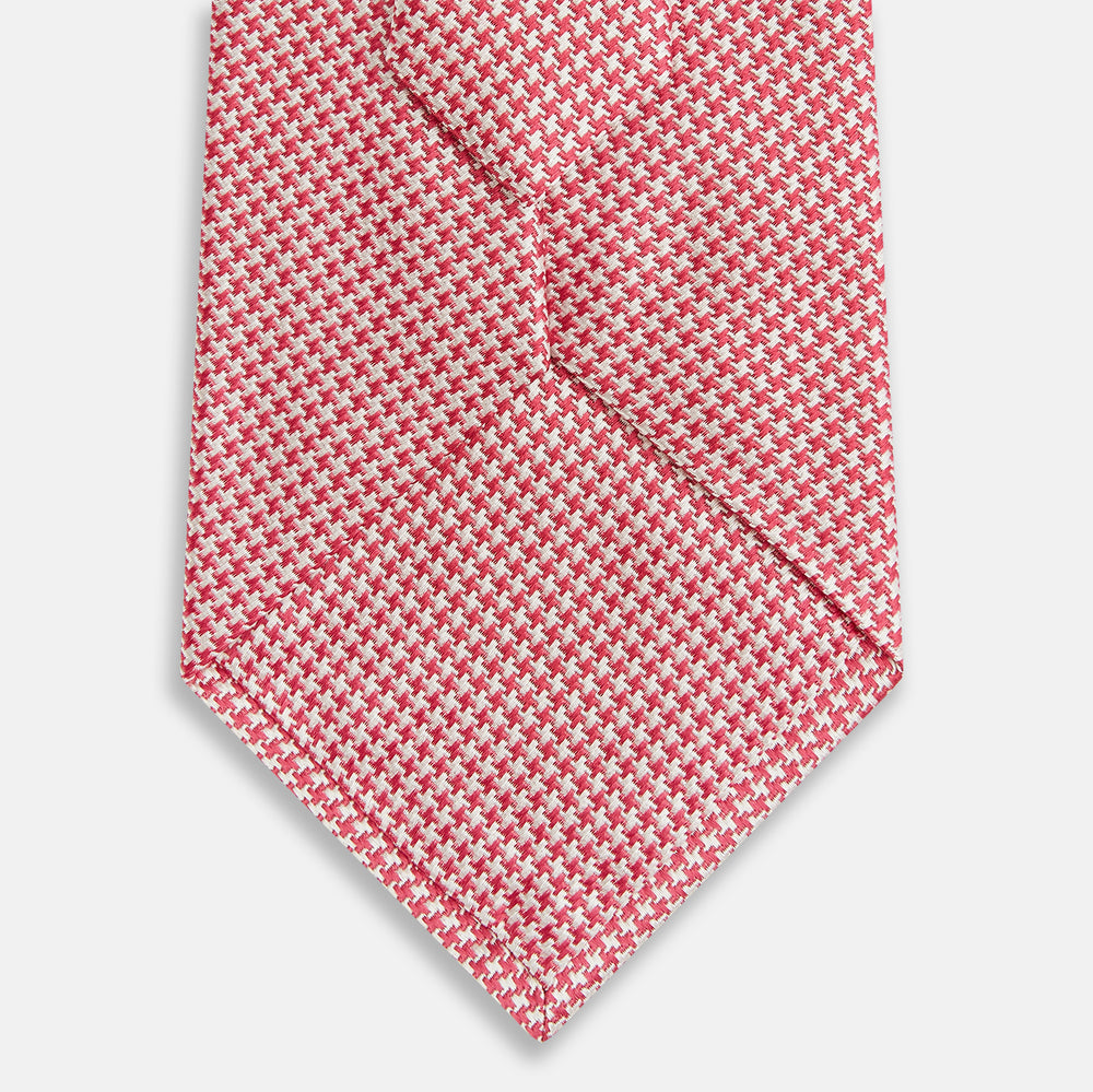 The Turnbull & Asser Pink and White Houndstooth Silk Tie features a small pattern and is displayed rolled up on a plain white background, making it perfect for pairing with any office shirt.