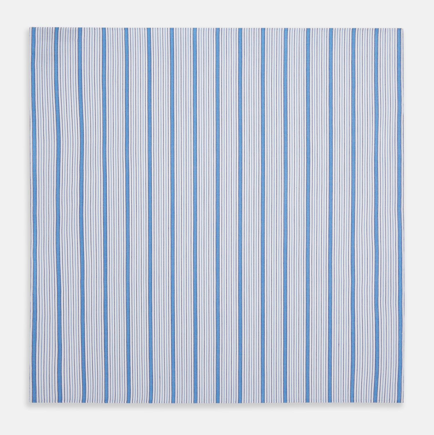 View 3 of product The Hand Rolled Blue Multi Track Stripe Handkerchief by Turnbull & Asser features a square white design with vertical light blue and navy stripes of varying widths—a timeless gentleman’s accessory.