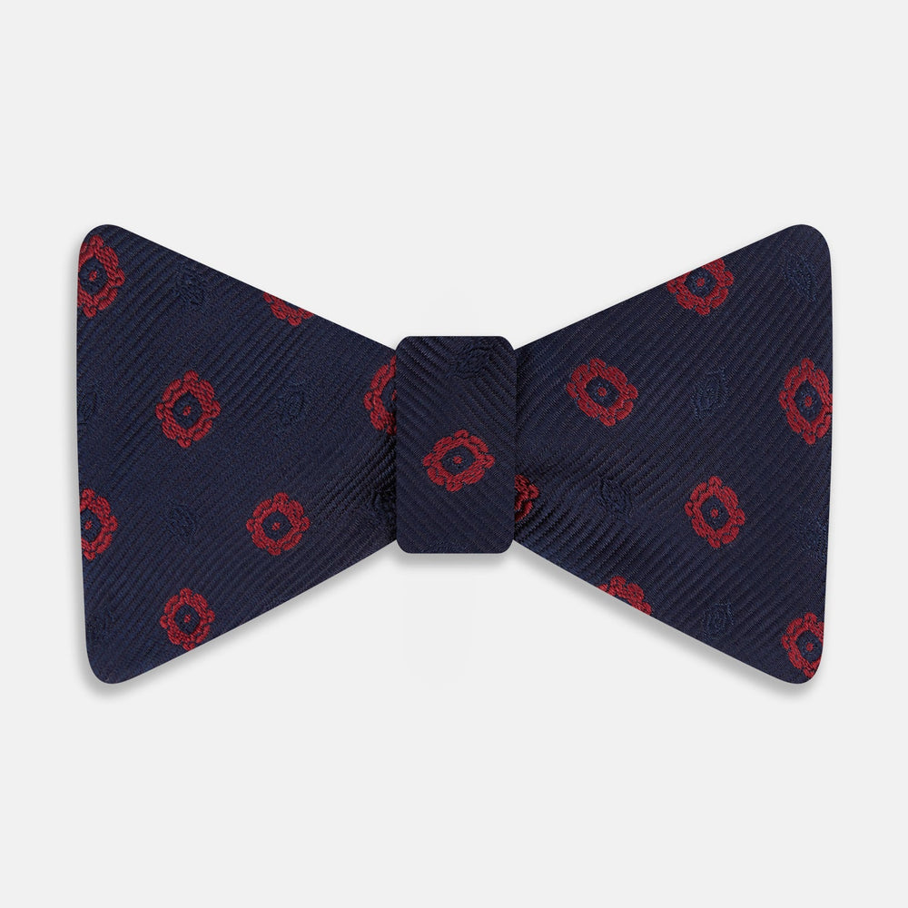 Elevate your formalwear with the Turnbull & Asser Navy and Burgundy Motif Silk Bow Tie, featuring a subtle ribbed texture and repeating red geometric motifs.