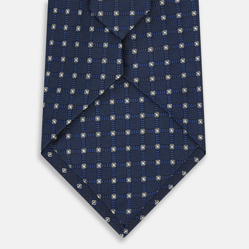The Turnbull & Asser Navy and White Geometric Silk Tie, featuring a micro pattern of light blue and white squares, is displayed rolled up on a plain white background.