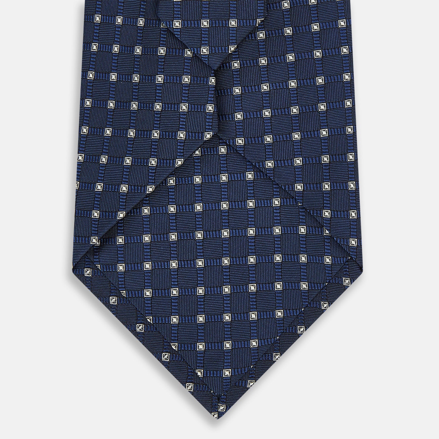 View 3 of product The Turnbull & Asser Navy and White Geometric Silk Tie, featuring a micro pattern of light blue and white squares, is displayed rolled up on a plain white background.