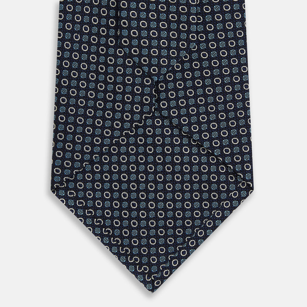 The Turnbull & Asser Blue and Cream Circle Silk Tie features a navy base with a repeating pattern of light blue and cream circles, shown on a plain white background for classic sophistication.